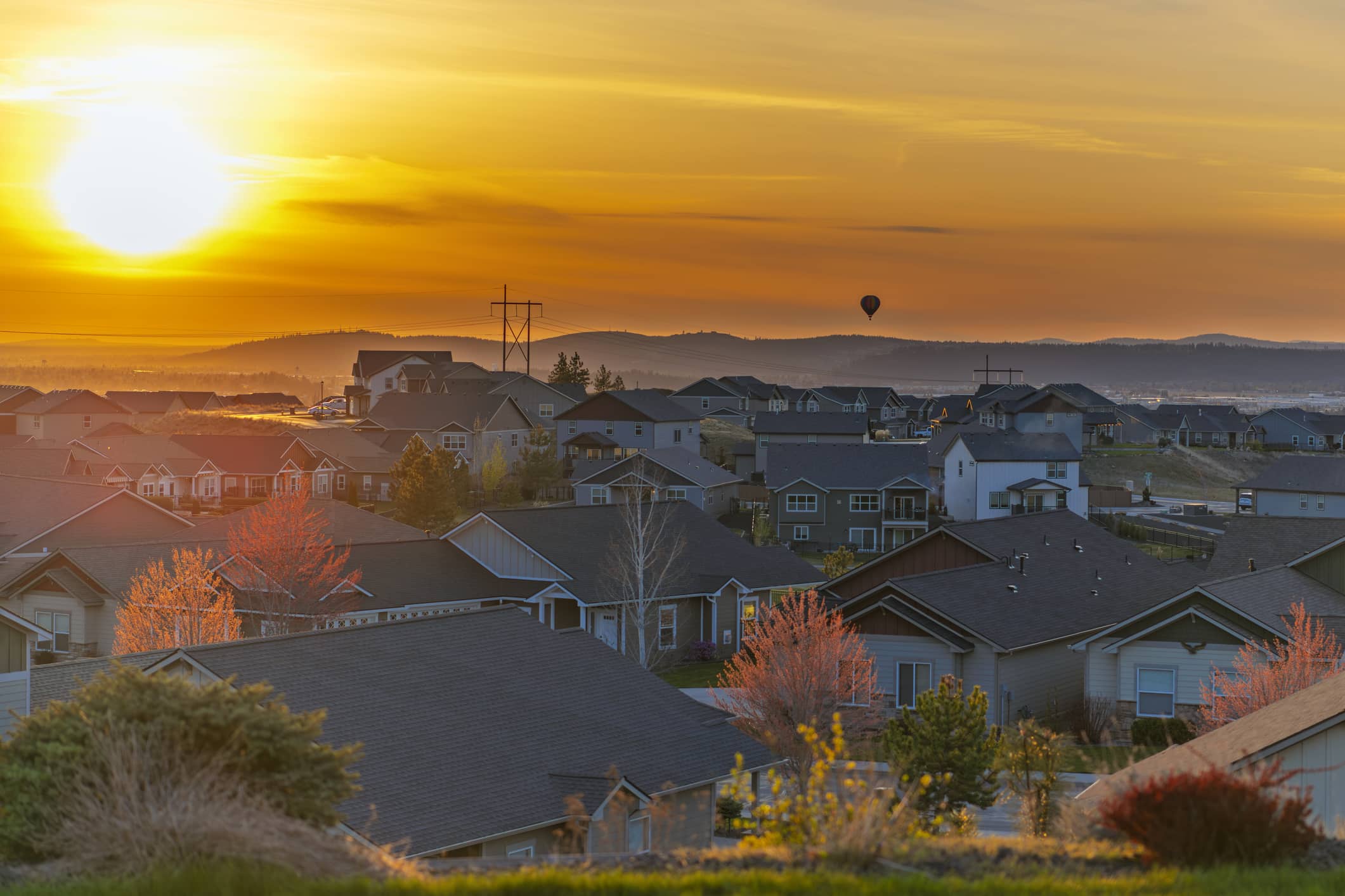 A hot air balloon flies over the city of Spokane and Spokane Valley, Washington, seen from a hillside neighborhood in the suburb of Liberty Lake at sunset.